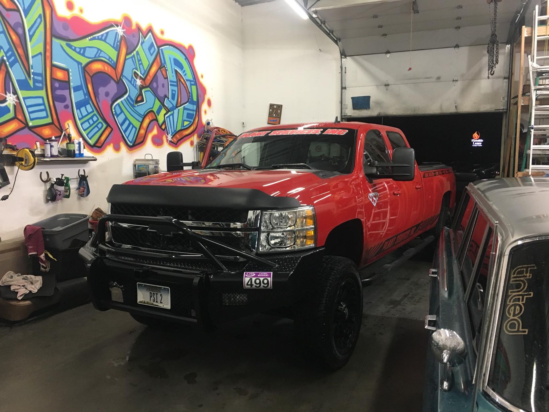 A red truck is parked in a garage with graffiti on the wall.