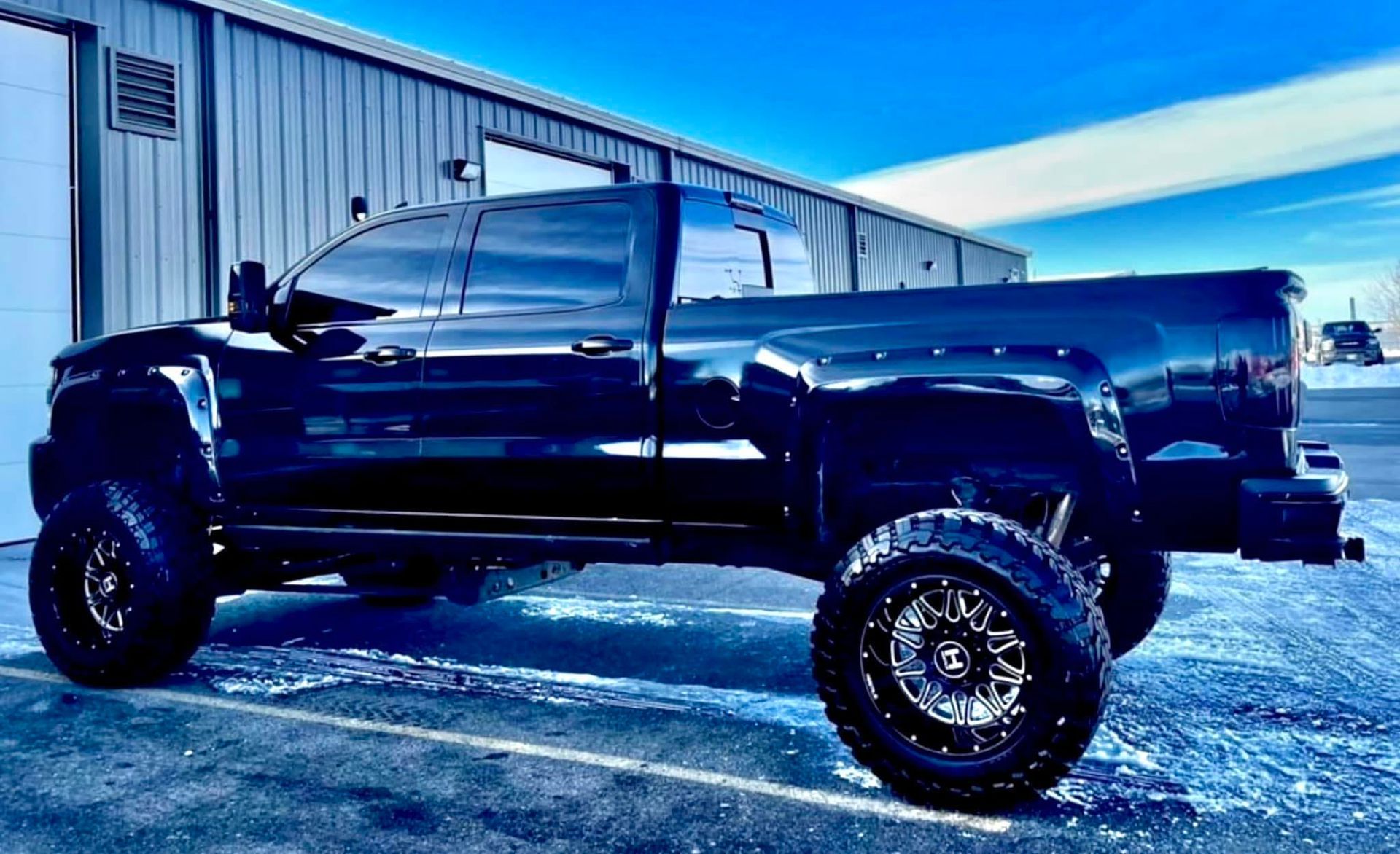 A black truck is parked in a parking lot in front of a building.
