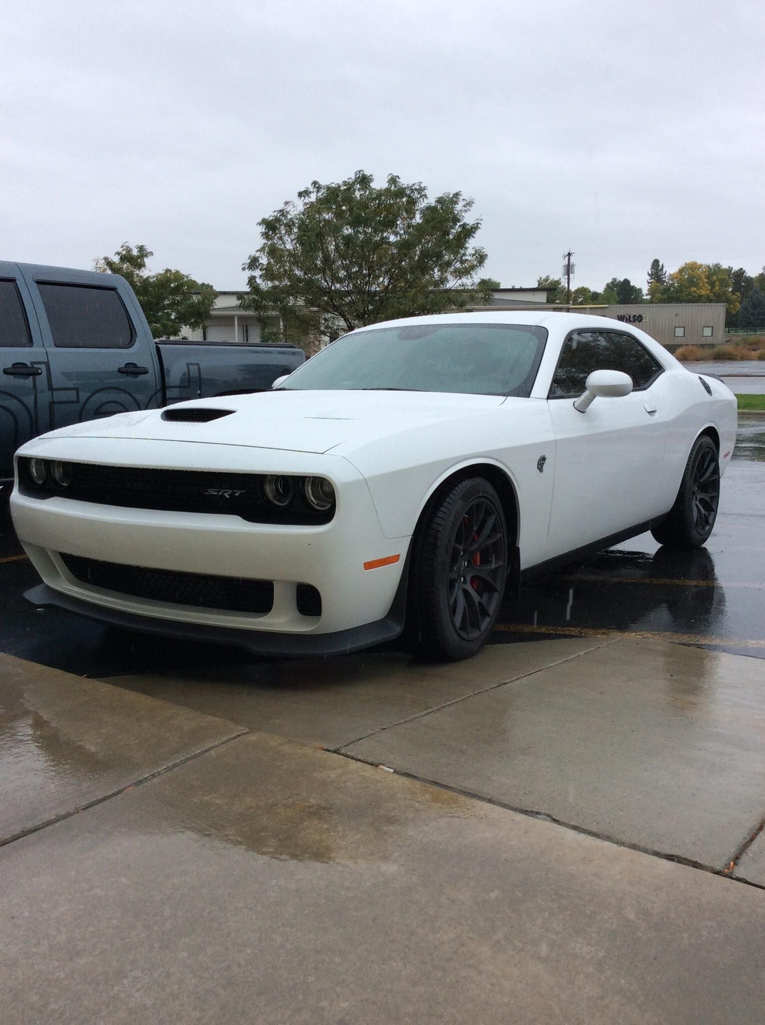 A white dodge challenger is parked in a parking lot on a rainy day.