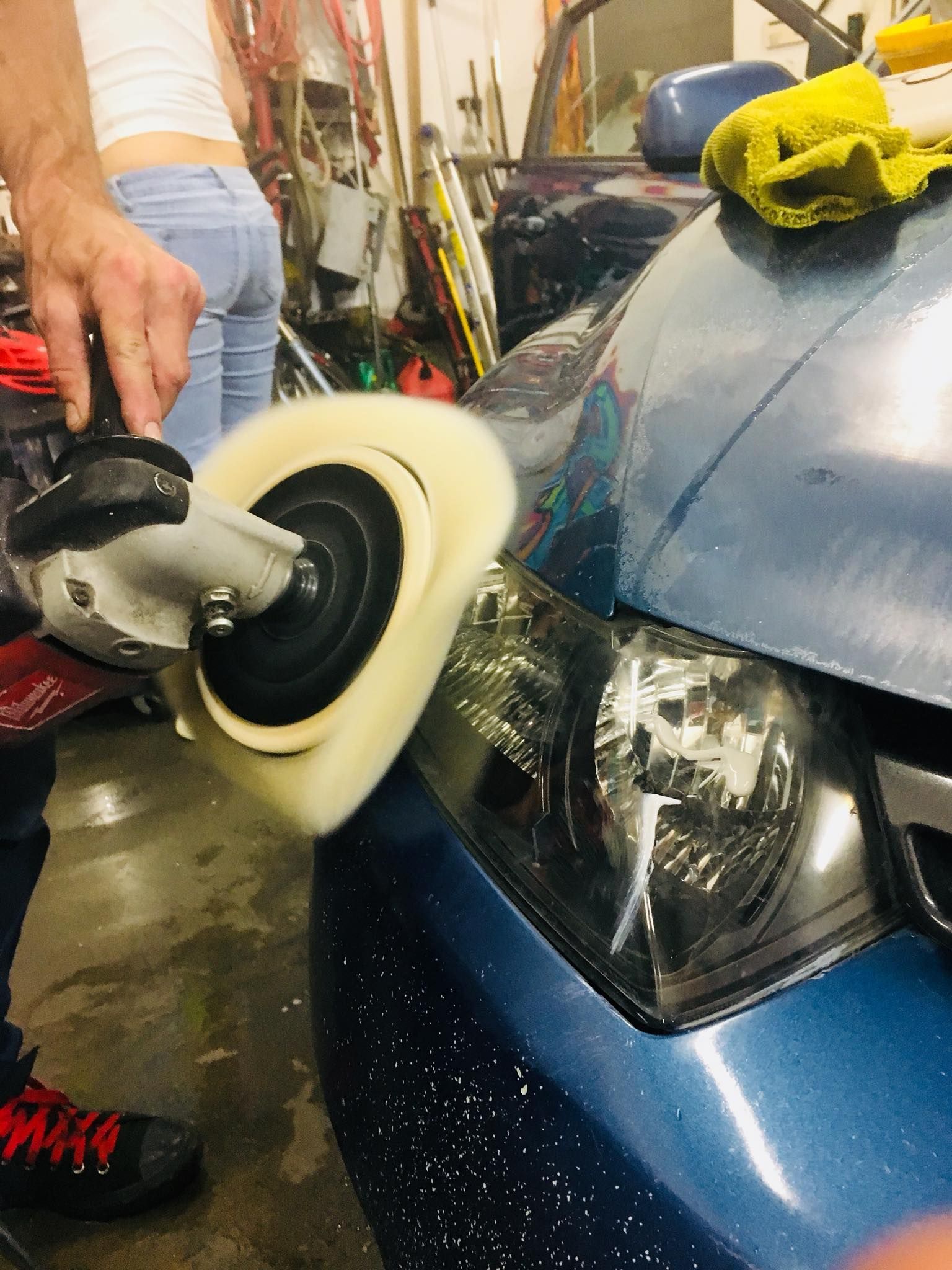 A man is polishing the headlights of a blue car