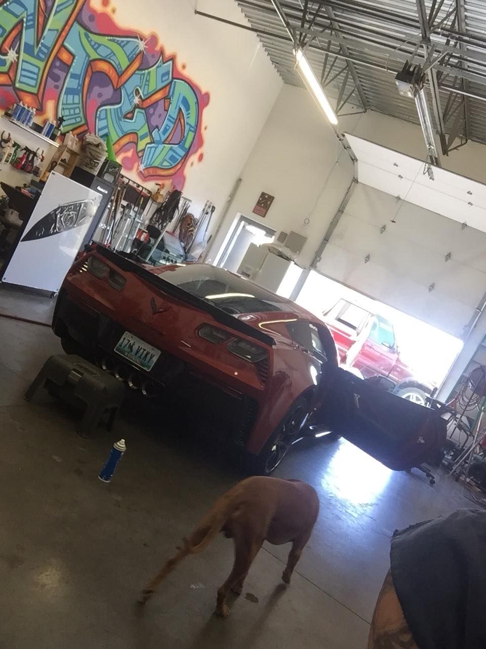 A red corvette is parked in a garage with graffiti on the wall behind it