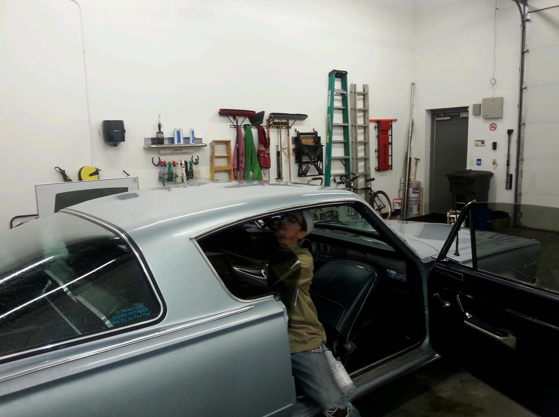 A man is standing next to a silver car in a garage
