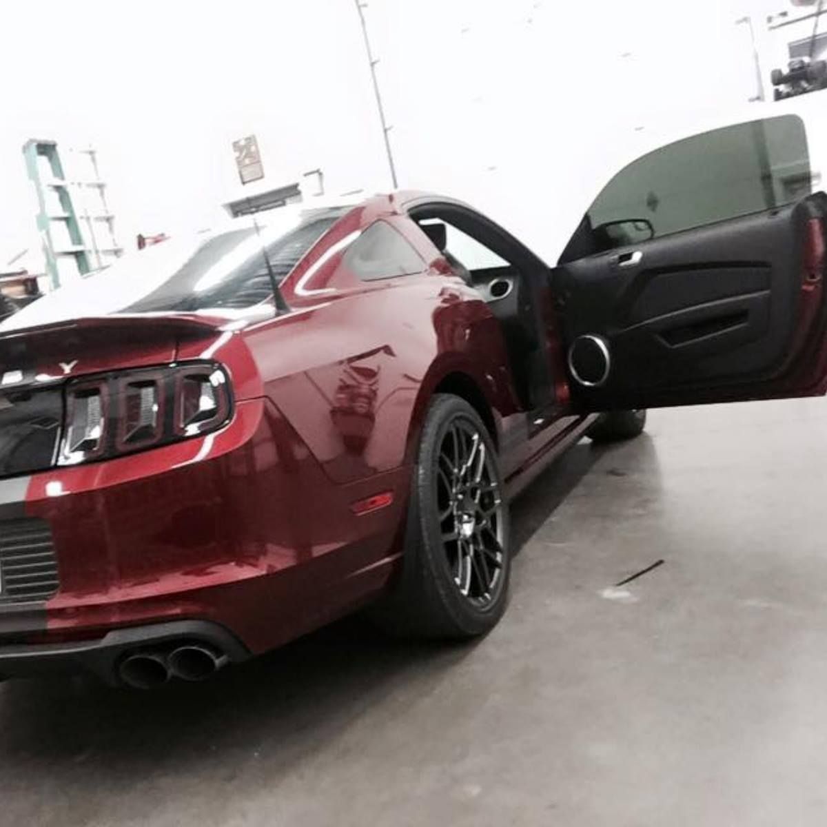 A red mustang is parked in a garage with its doors open