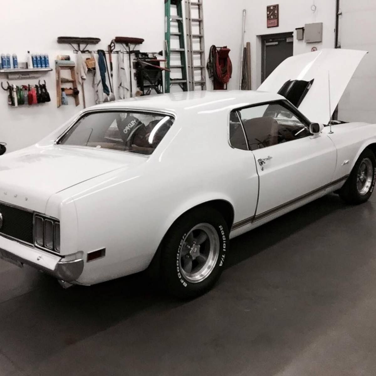 A white car with the hood up is parked in a garage