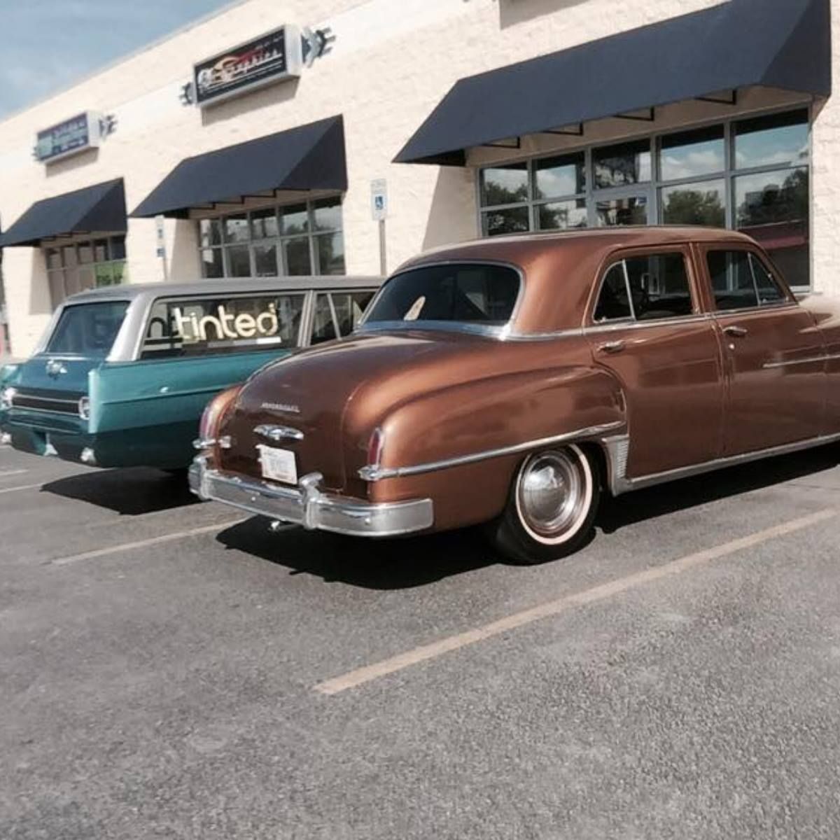 Two old cars are parked in front of a building that says linked