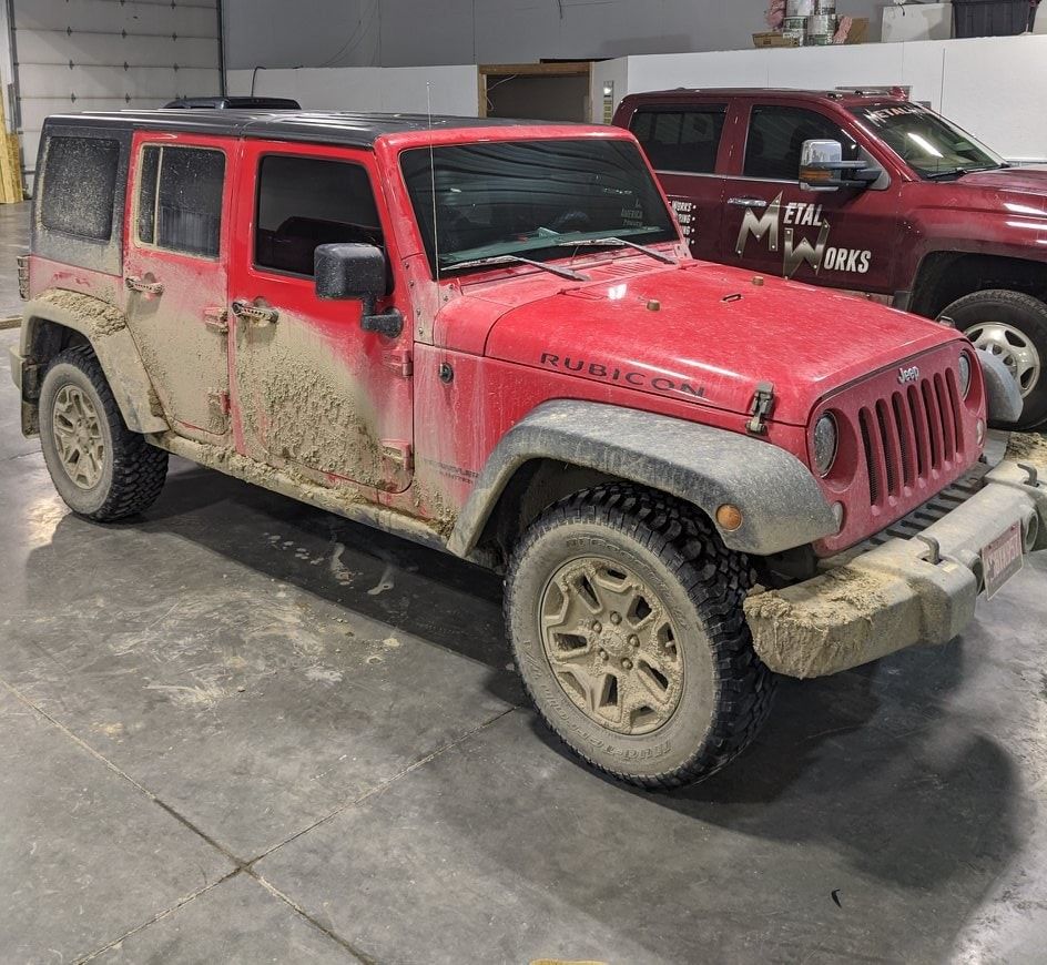 A muddy red jeep is parked in a garage.