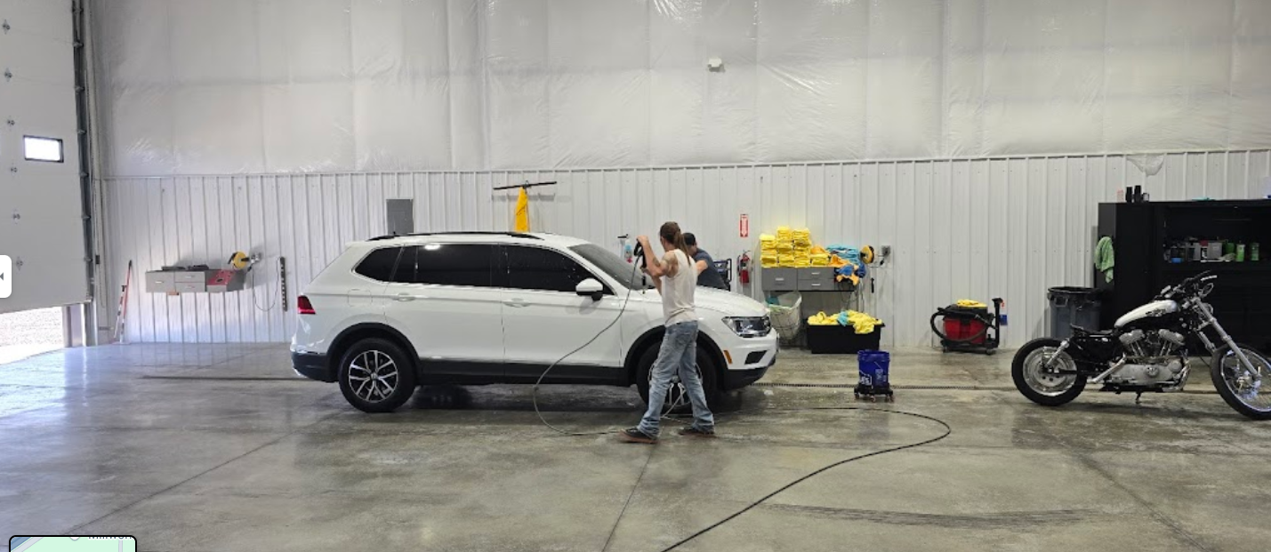 A man is washing a white suv in a garage next to a motorcycle.