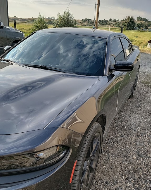 A black dodge charger is parked on a gravel road.