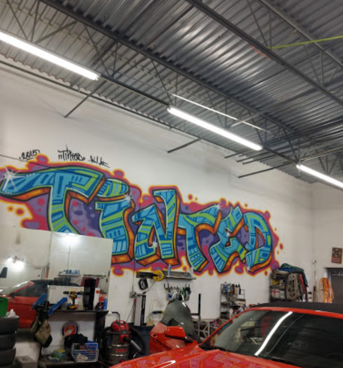 A red car is parked in front of a wall that has graffiti on it