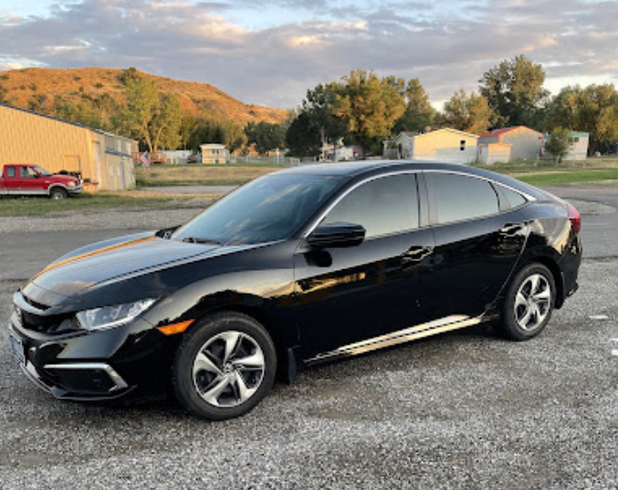 A black honda civic is parked in a gravel lot.
