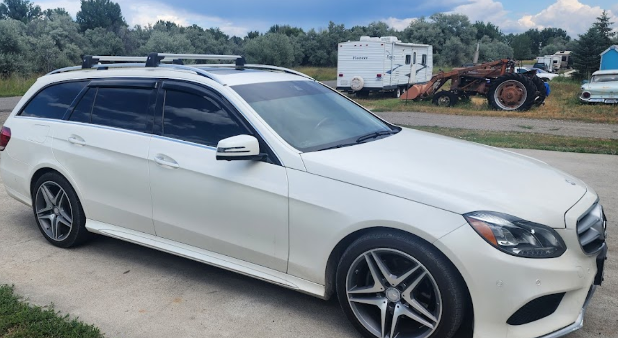 A white mercedes benz e class station wagon is parked on the side of the road.