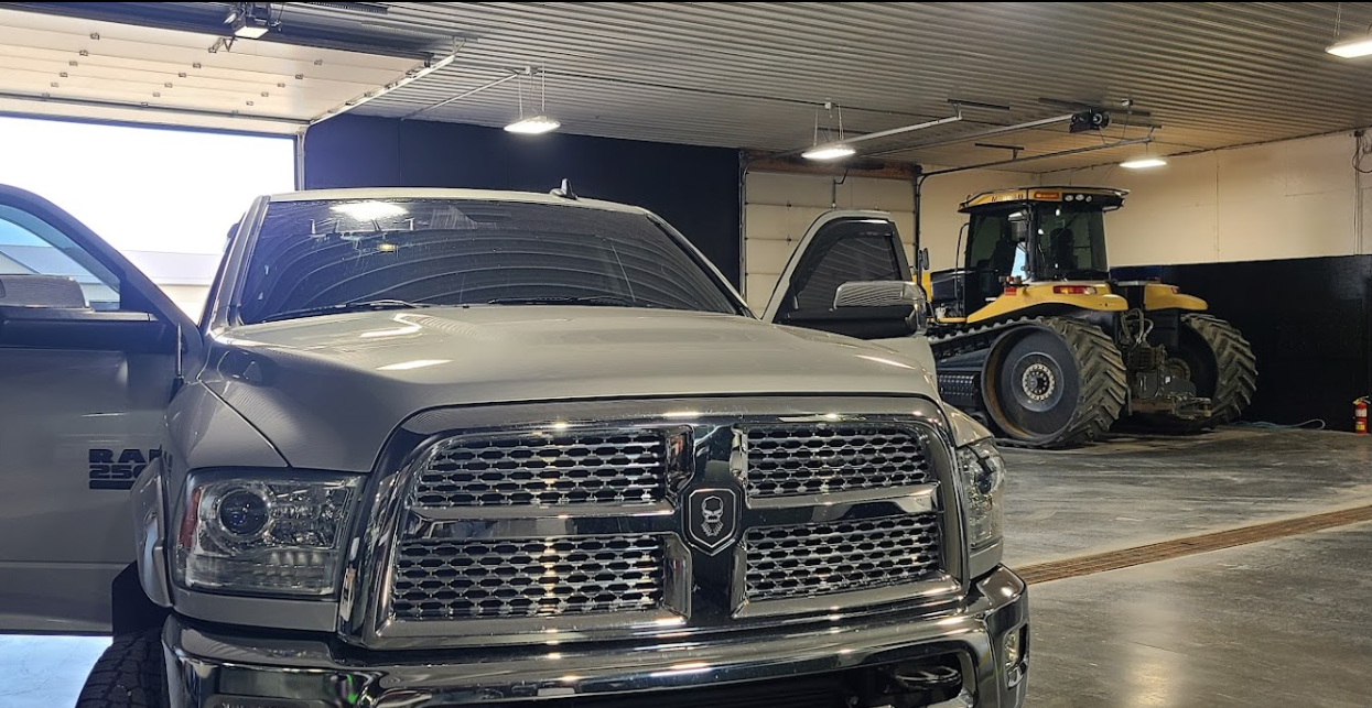 A ram truck is parked in a garage with a bulldozer in the background.