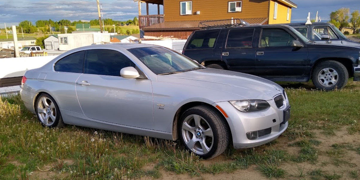A silver car is parked next to a black suv in a grassy field.