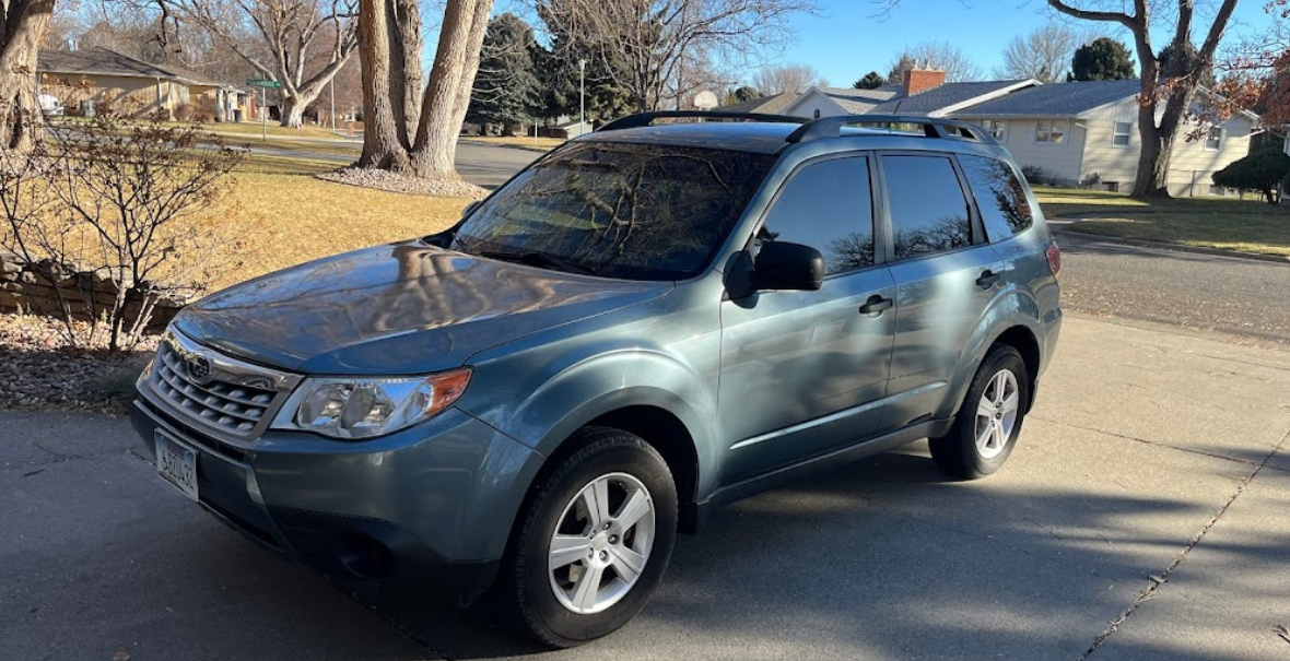 A blue suv is parked in a driveway in front of a house.