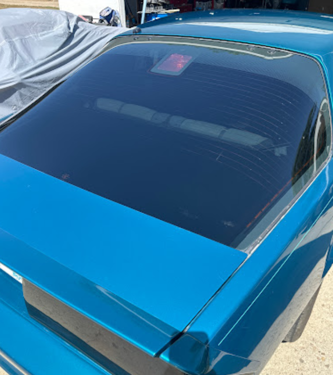 A blue car with a black windshield is parked in a garage.