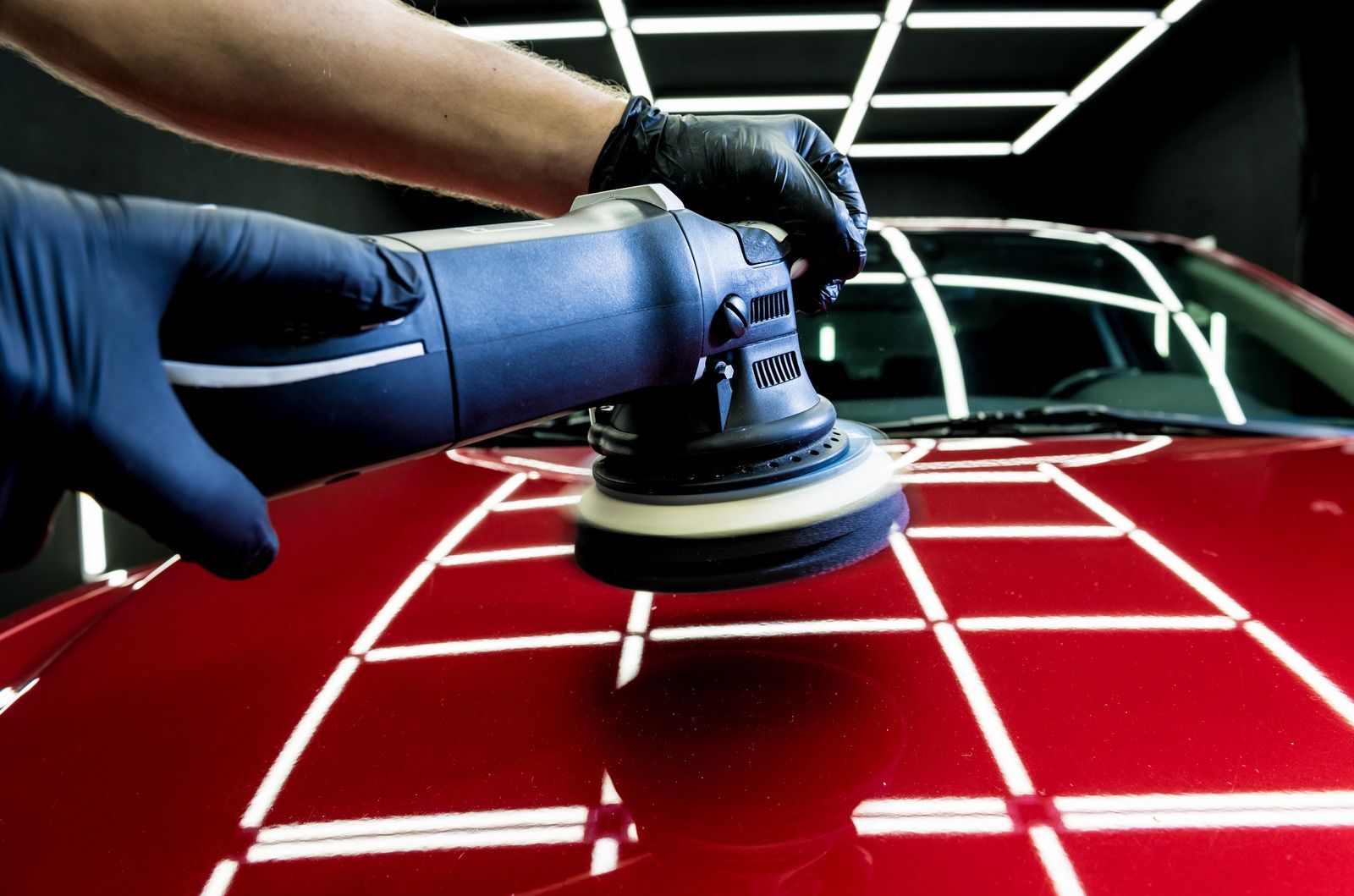 A person is polishing a red car with a machine.