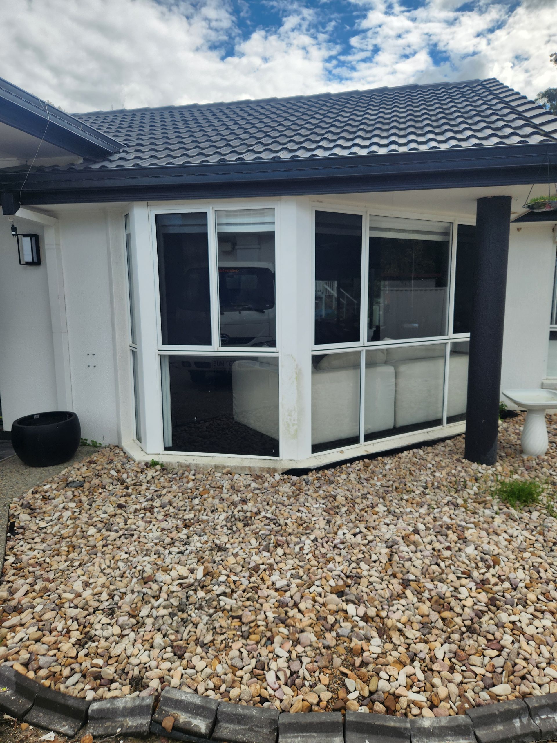 A white house with a rock garden, bay window, and black roof under a partly cloudy sky — Smart Screens Qld in Ormeau, QLD
