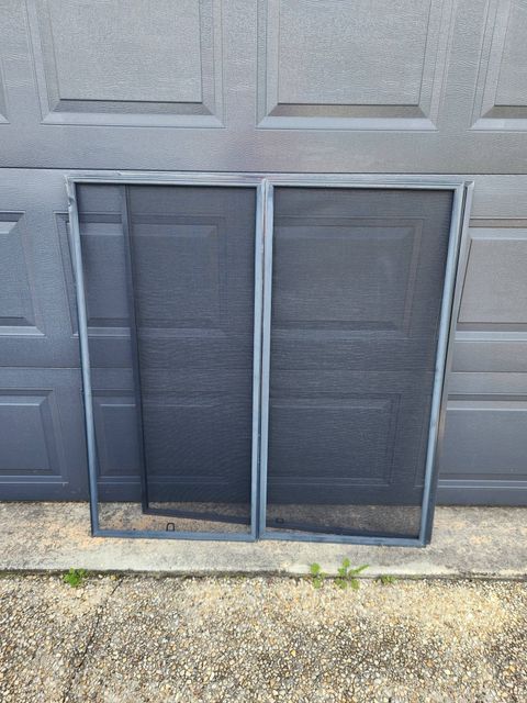 Two Dark Gray Window Screens Leaning Against a Gray Garage Wall Near a Door — Smart Screens Qld in Ormeau, QLD