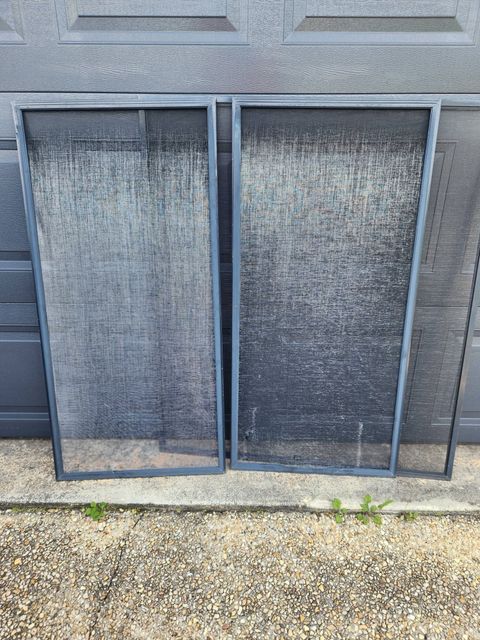 Two Weathered Window Screens Leaning Against a Gray Exterior Wall on Gravel — Smart Screens Qld in Ormeau, QLD