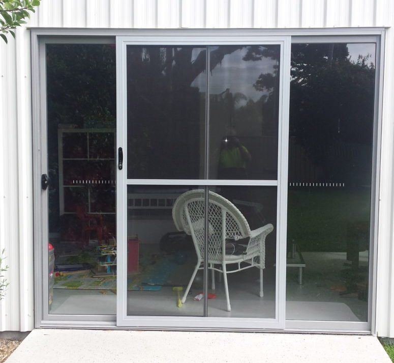 A Wicker Chair Sits in Front of A Sliding Glass Door — Smart Screens Qld in Ormeau, QLD