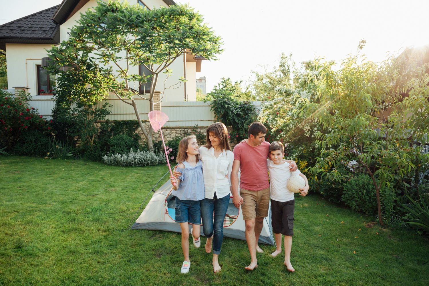 Family walking through a sunny backyard, toward the camera. A tent is set up on the lawn.