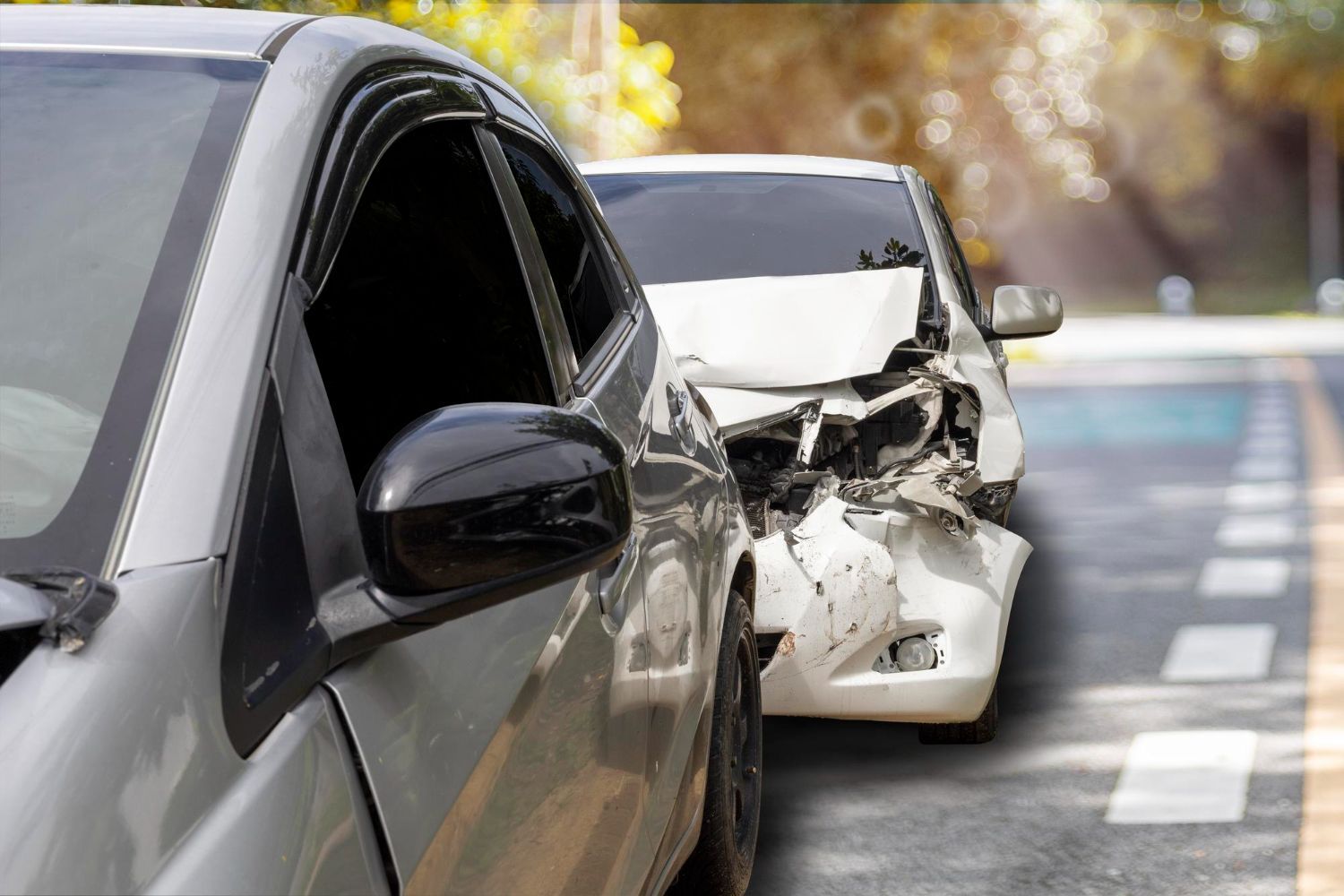 Two cars, one silver, one white, involved in a collision on a road. The white car is heavily damaged.
