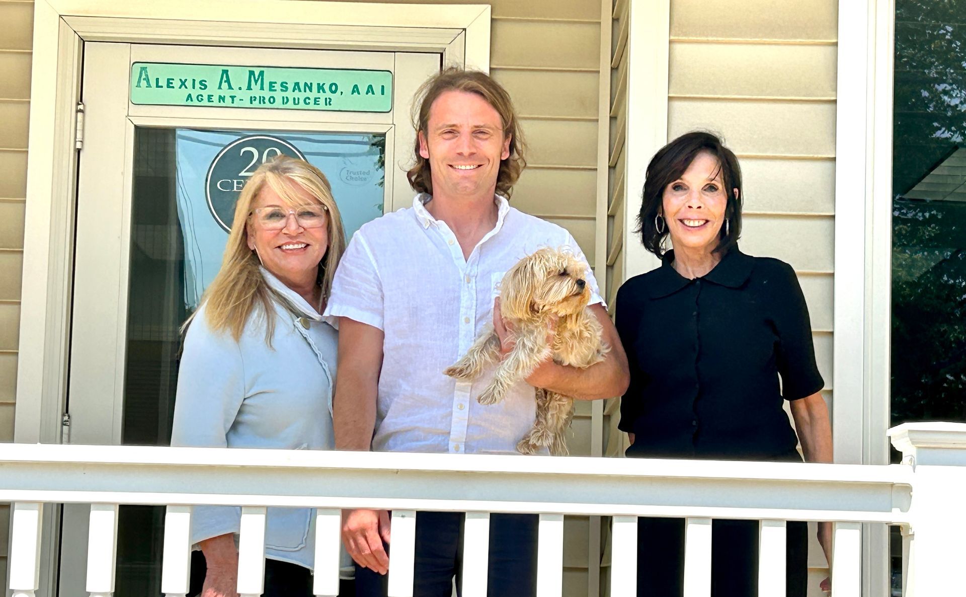 Three people and a dog on a porch; a sign says 