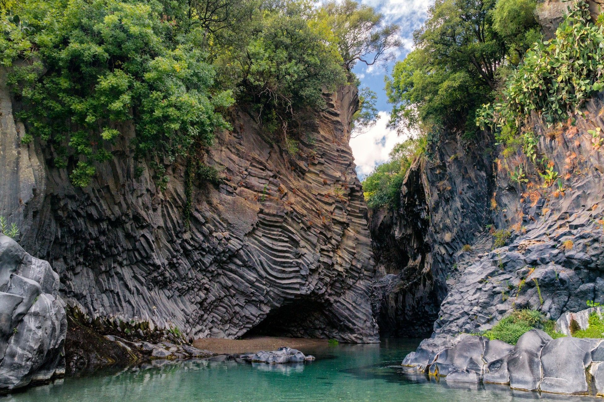 Una grotta nel mezzo di una scogliera rocciosa vicino ad uno specchio d'acqua.