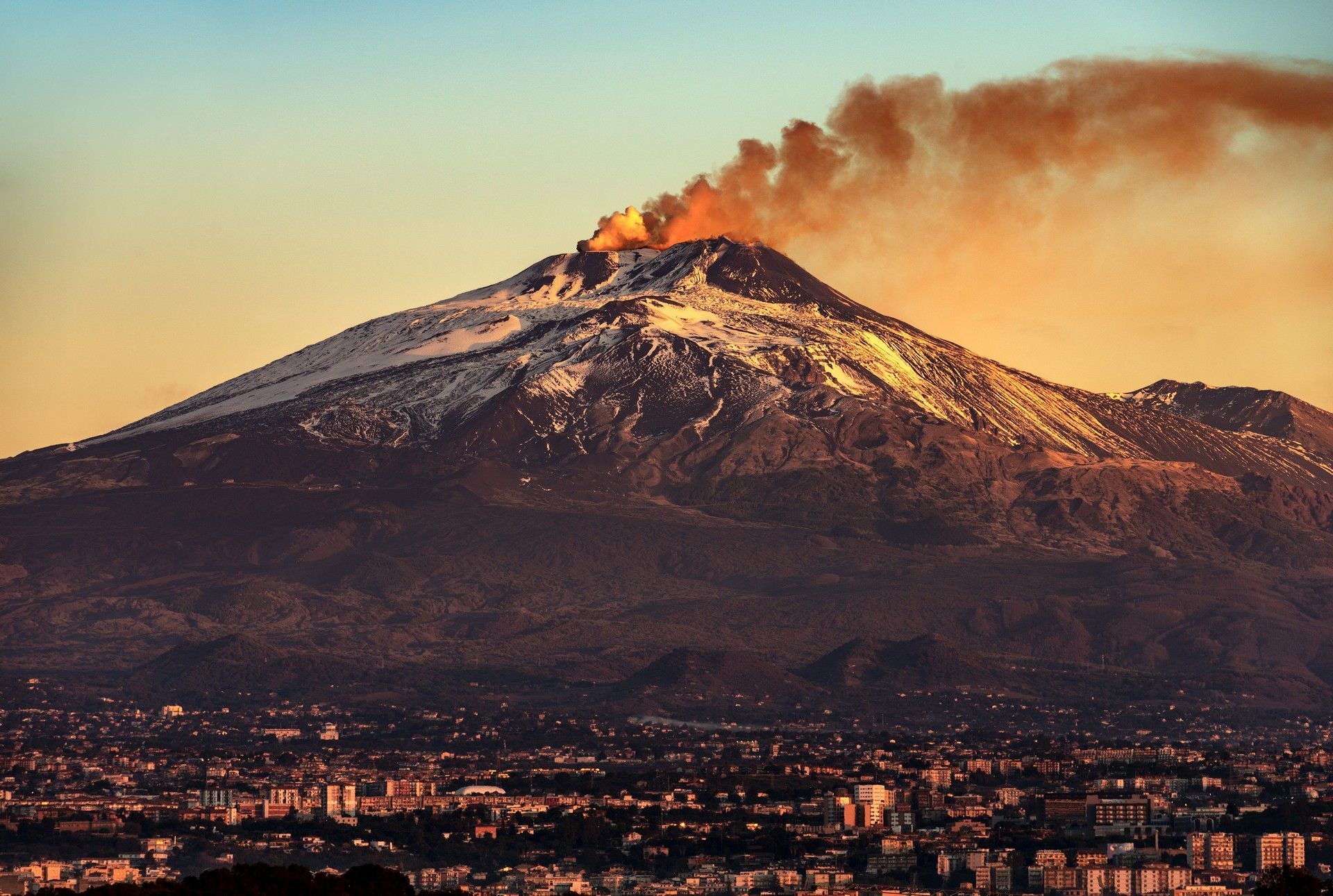 Un vulcano dal quale esce fumo e una città in primo piano