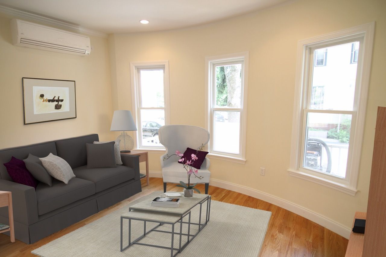 Living room in an apartment with a gray sofa, armchair, coffee table, and large windows.