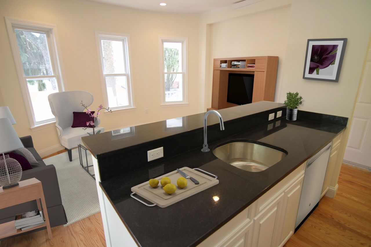Open-concept kitchen with a dark countertop island and sink, with living area in the background.