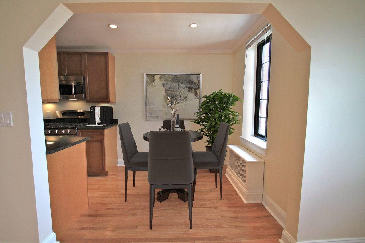 Interior apartment dining area with a round table, gray chairs, and a window with a plant.