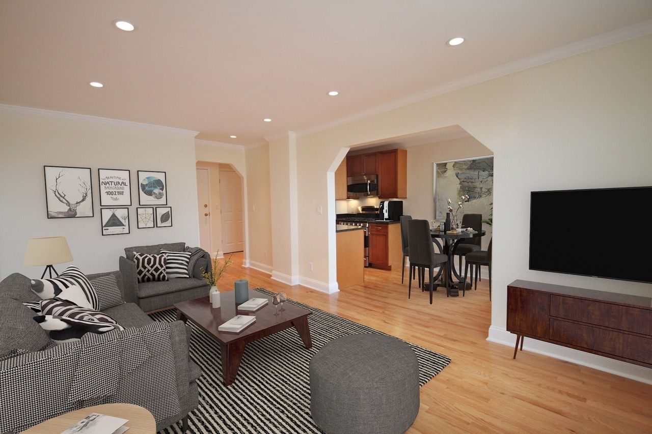 Open-concept living room with gray sofa, coffee table, and a TV, adjacent to the kitchen.