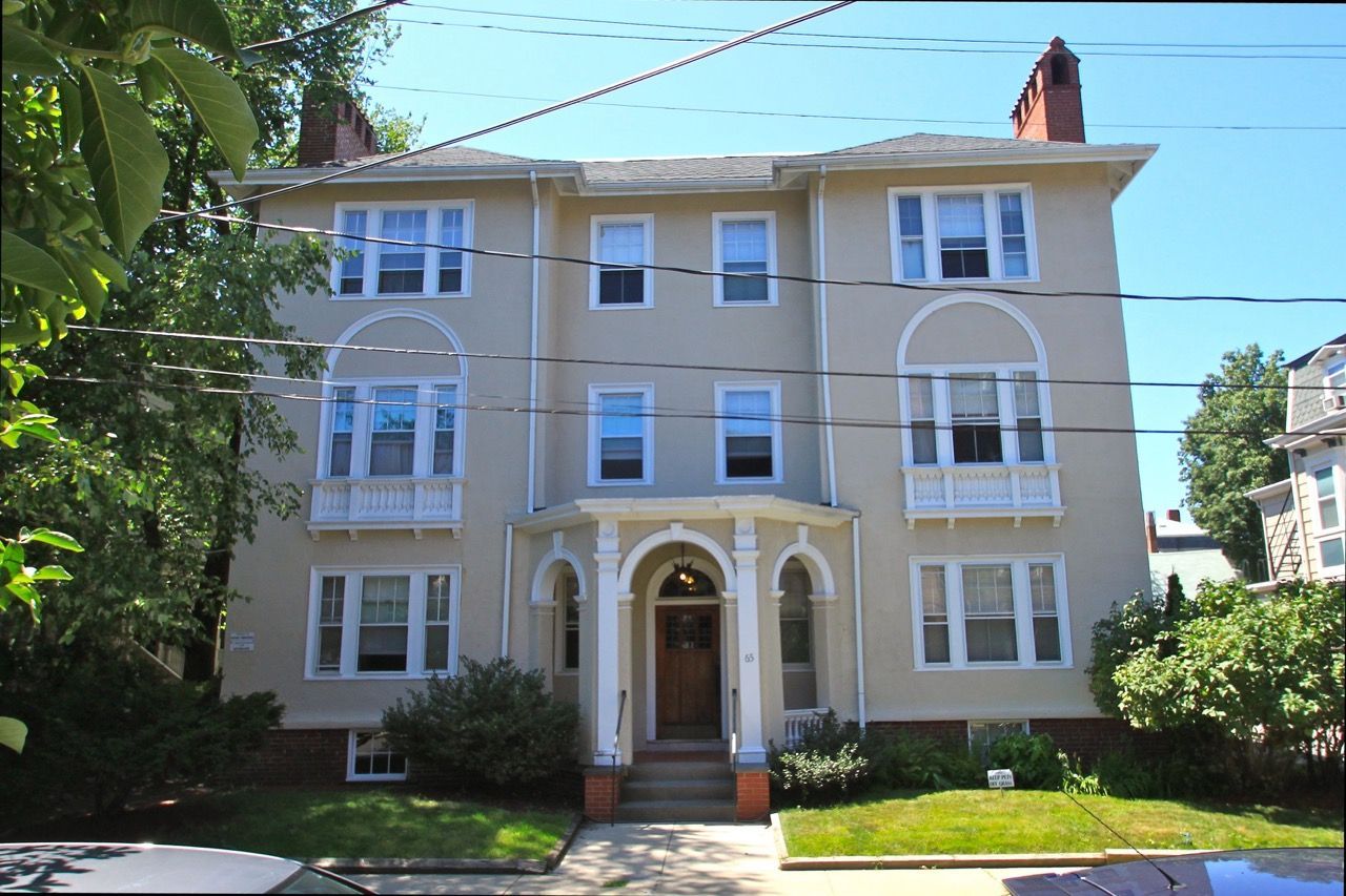 Three-story beige apartment building with arched windows and a columned front entrance.