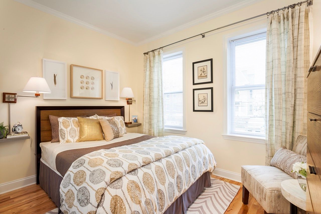 Bedroom in an apartment with a queen bed, wall art, and two windows.