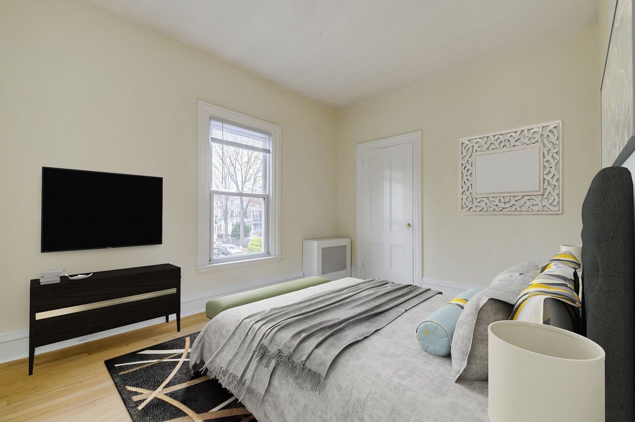 Bedroom in an apartment with a bed, dresser, wall-mounted TV, and a window.