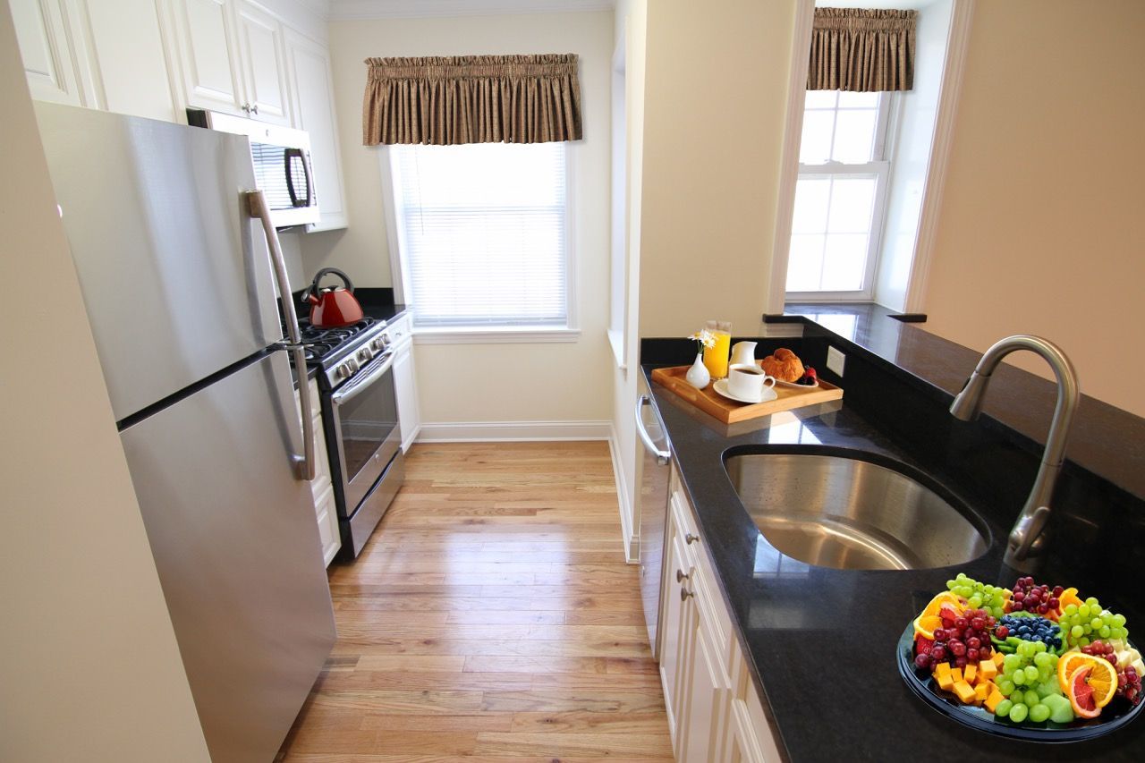 Bright apartment kitchen with stainless-steel fridge, stove, and a curved sink on a dark countertop.