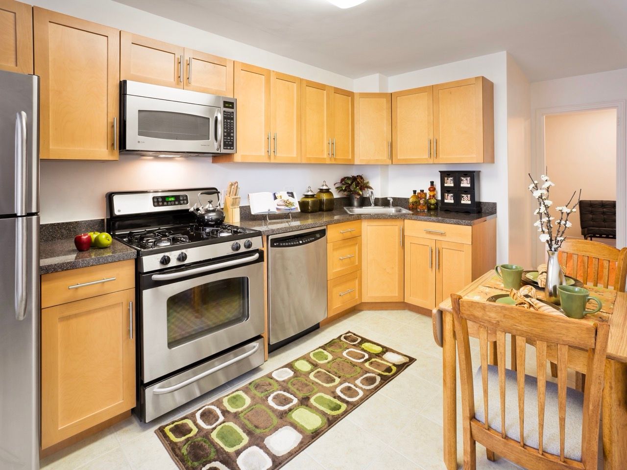 Bright apartment kitchen with light wood cabinets, stainless steel appliances, and a dining table.