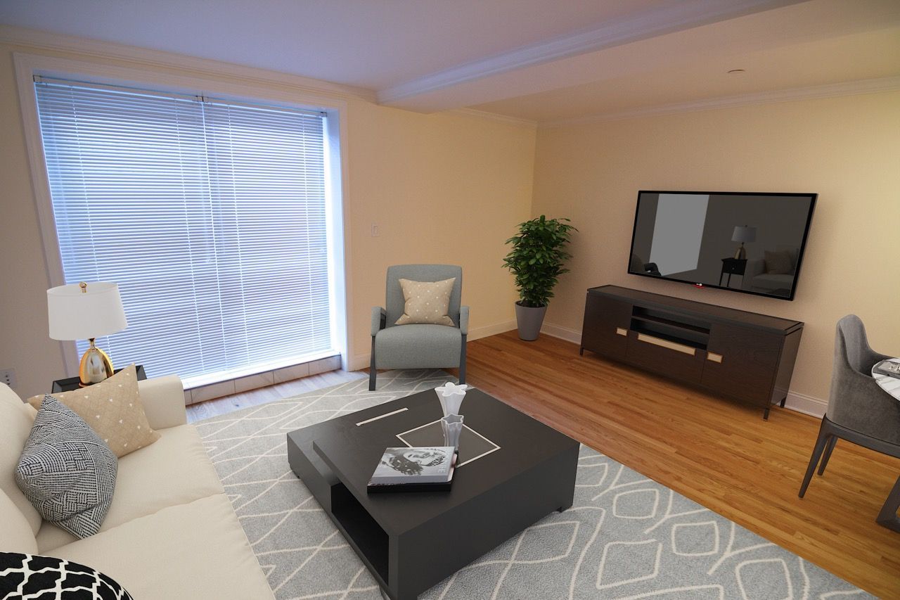Living room in an apartment with sofa, coffee table, TV, chair, plant, and blinds.