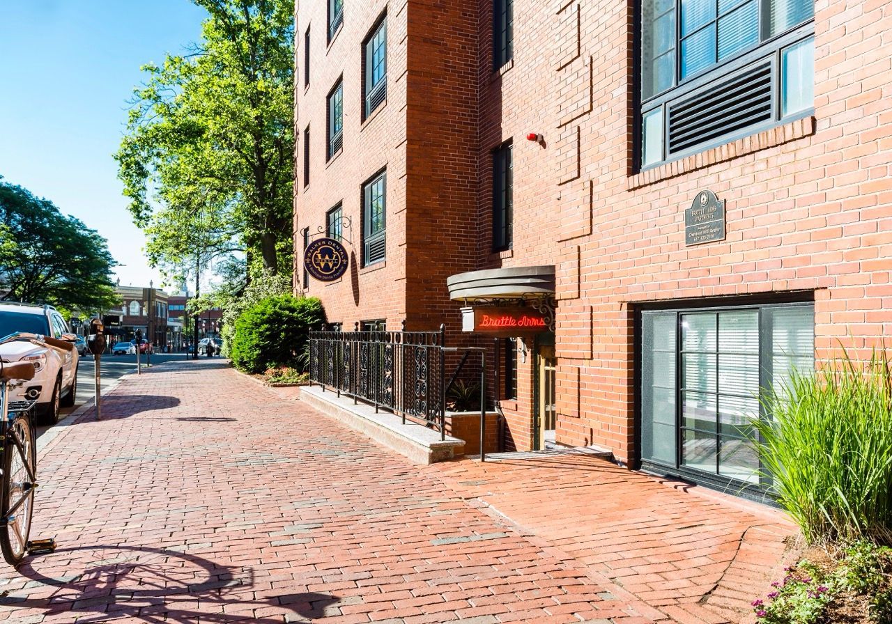 Exterior view of a brick apartment building with sidewalk and signage.