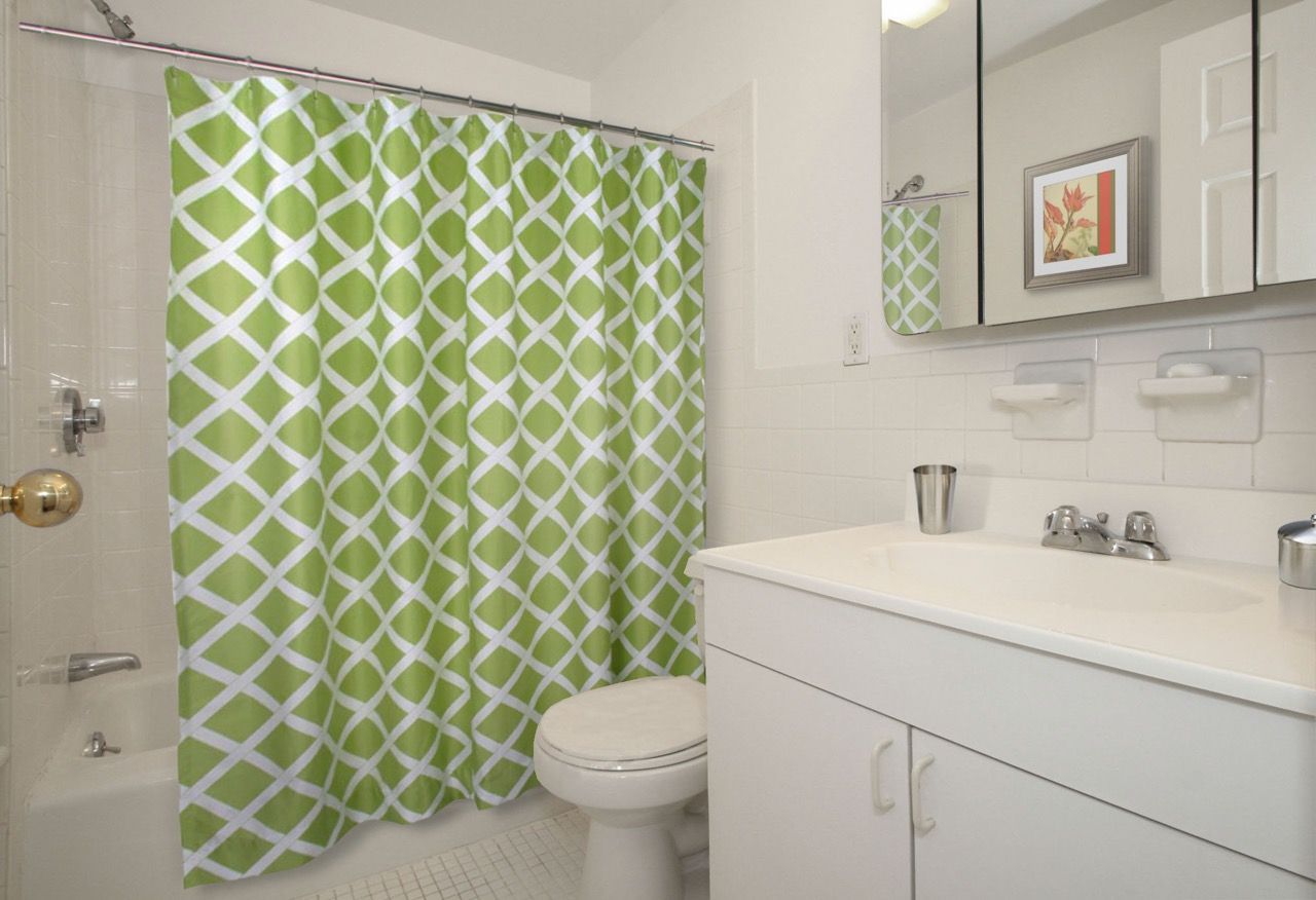 Bathroom interior with a white vanity, tiled walls, green geometric shower curtain, toilet, and mirror.