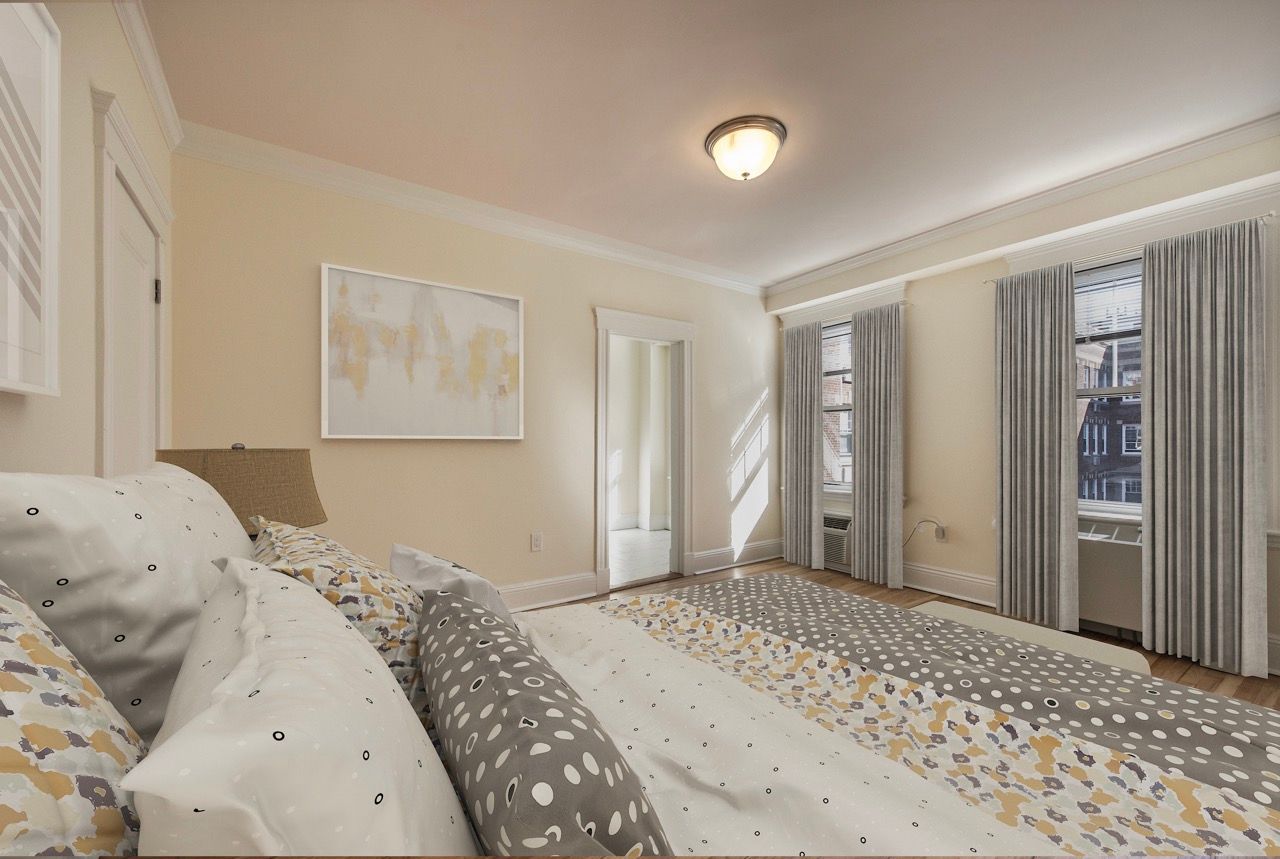 Bright bedroom with a large bed, beige walls, and tall windows with light curtains.