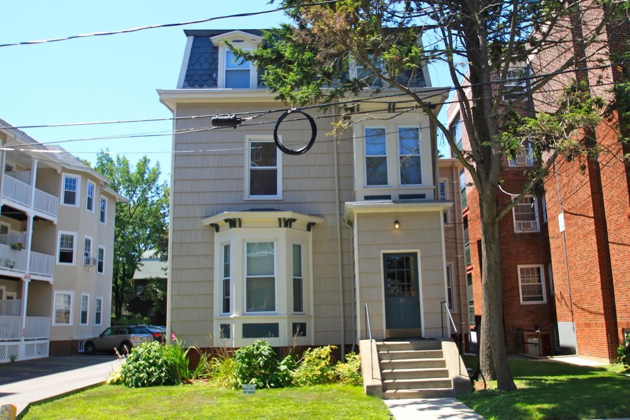 Exterior view of a townhouse-style apartment building with a bay window and front steps.