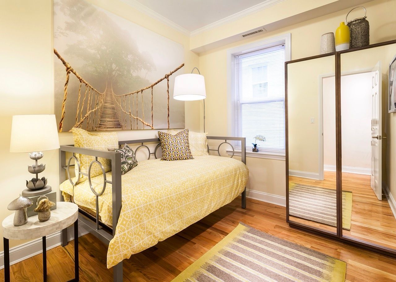 Bedroom in a modern apartment with yellow bedding, a metal-framed bed, and a mirrored wardrobe.