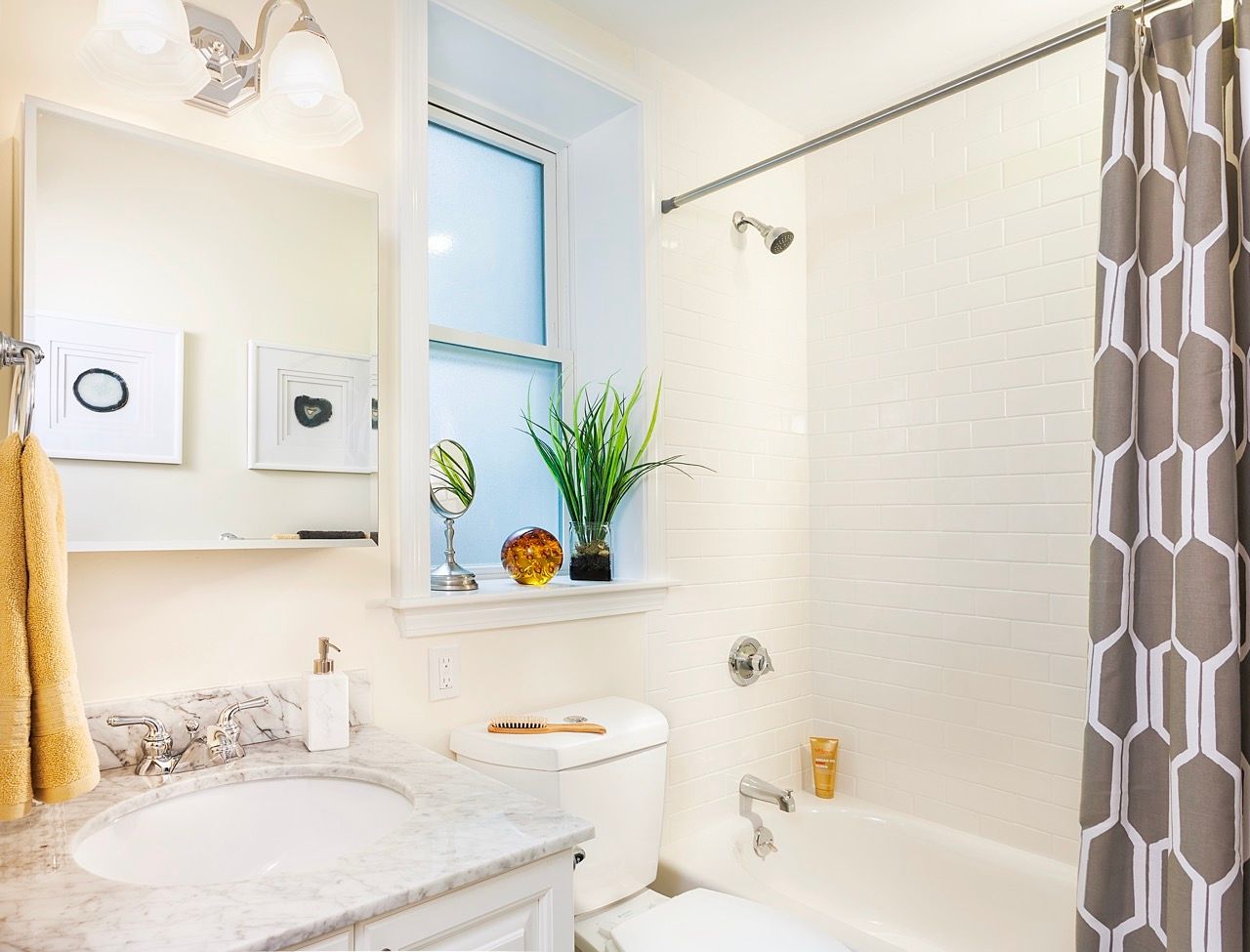 Bright bathroom with marble vanity, white tiles, tub/shower, and a gray patterned shower curtain.