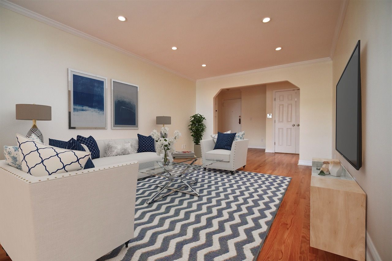 Bright living room with white sofa and chairs, blue pillows, chevron rug, and mounted TV.