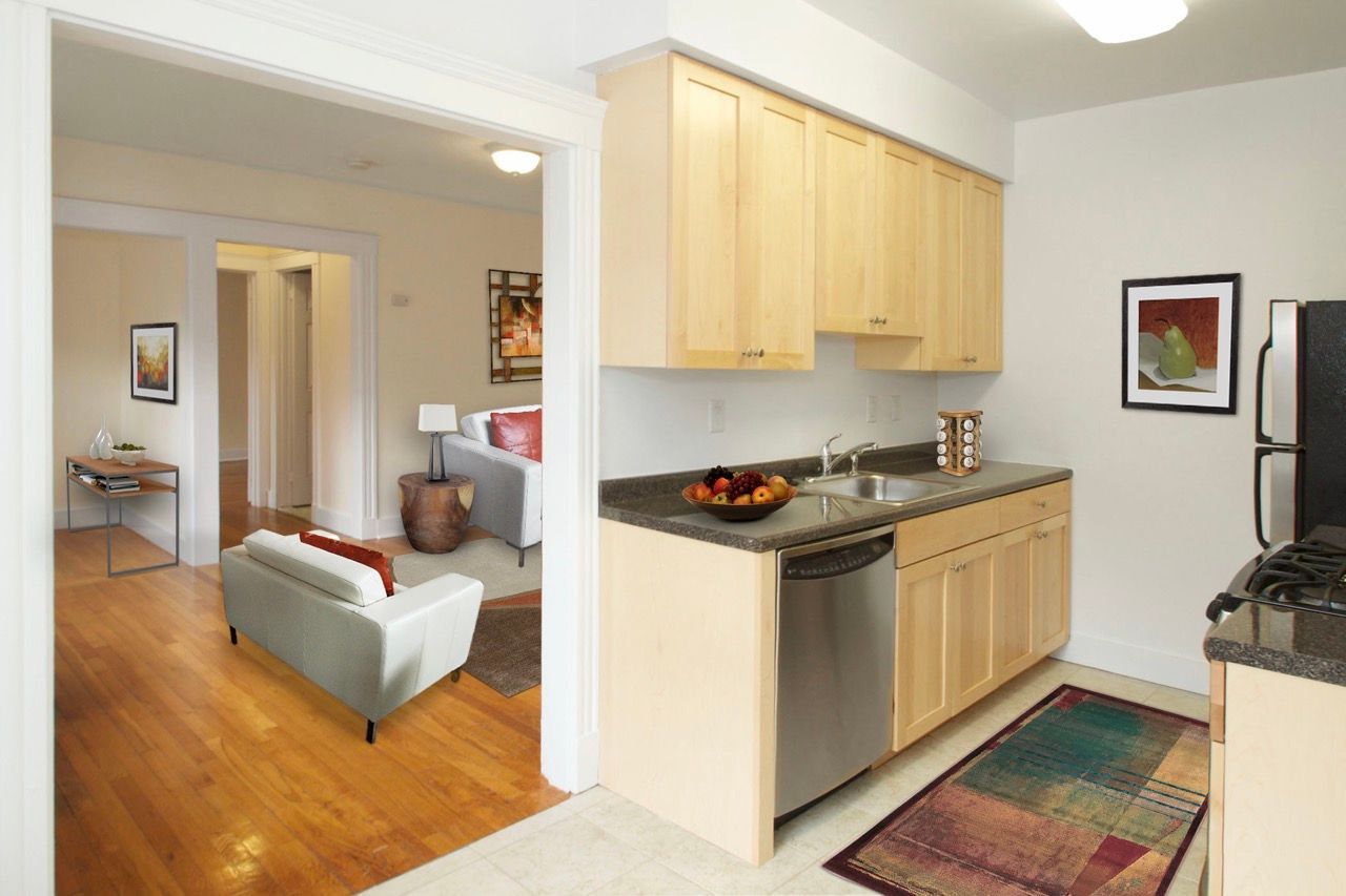 Kitchen with light wood cabinets, stainless dishwasher, double sink, and view into the living area.