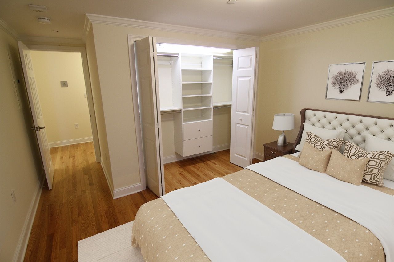 Bedroom with a white tufted headboard, nightstand, and an open built-in closet with shelves and drawers.