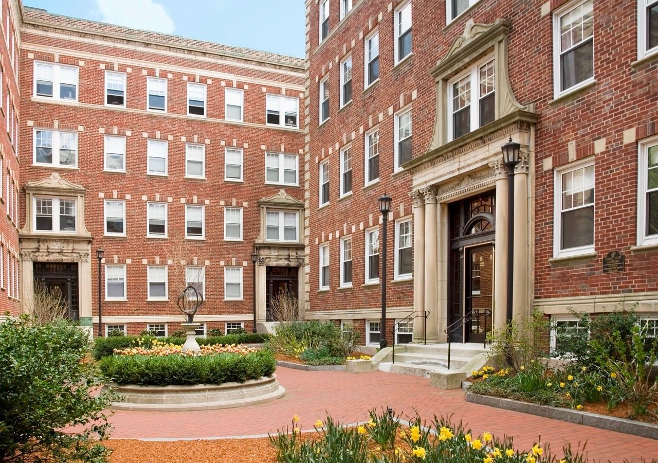 Courtyard view of a brick apartment complex with landscaped garden and entry stairs.