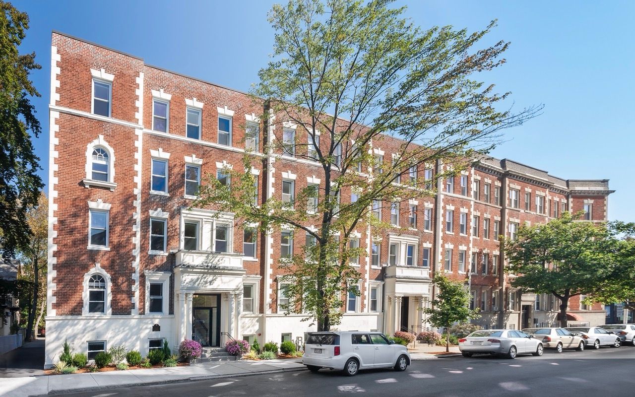 Brick apartment buildings on a tree-lined city street with parked cars.